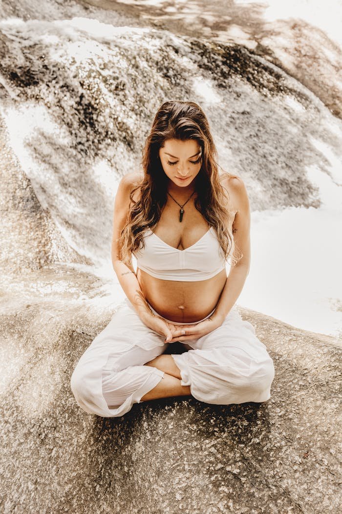 Tranquil scene of a pregnant woman meditating near a waterfall, embracing serenity and nature.
